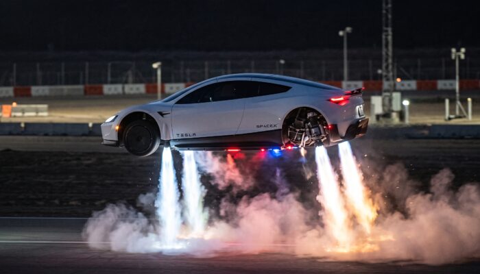 Tesla Roadster prototype hovering above an outdoor launch track with glowing SpaceX cold-gas thruster plumes